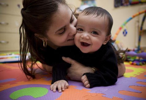 Woman kisses baby on the cheek while they play on the floor