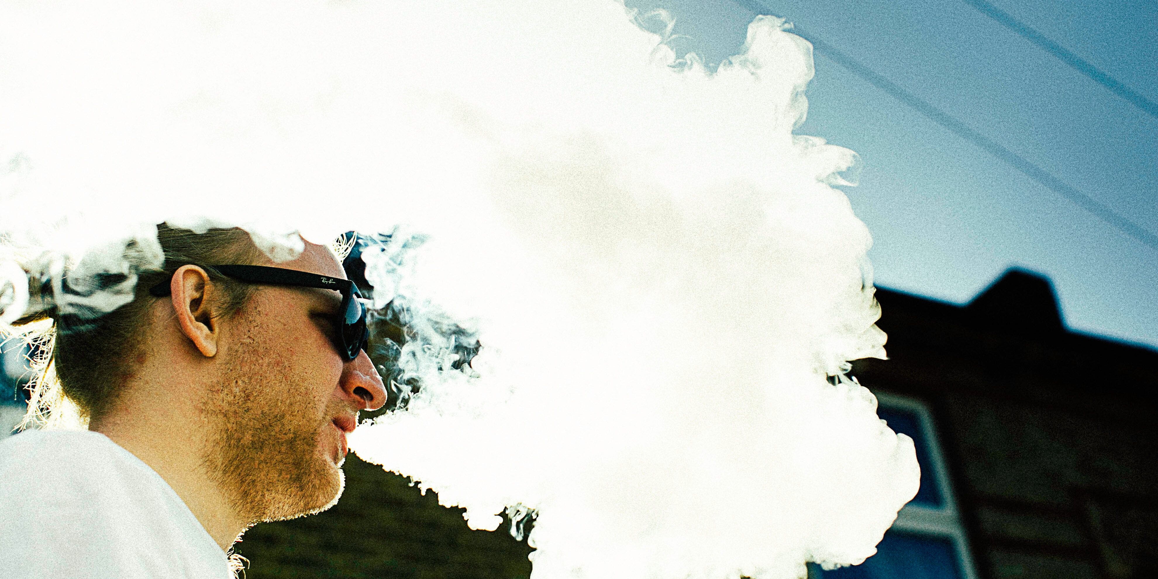 man wearing sunglasses blowing vape smoke